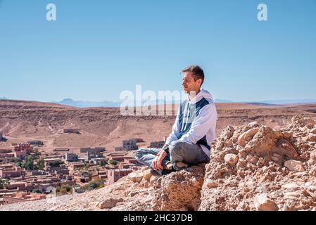 Jeune homme admirant la vue tout en étant assis sur le rocher contre la terre déserte et le ciel Banque D'Images