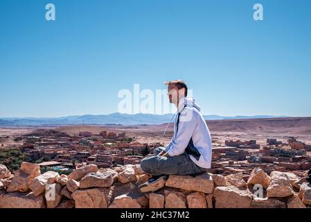 Jeune homme assis sur la pierre contre une vue panoramique sur la terre déserte et le ciel Banque D'Images