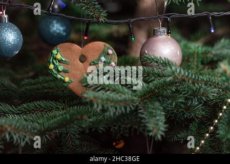Décorations de Noël accrochées à un sapin naturel.Boules de Noël, pains d'épices et chaînes décorés à la main sur l'arbre de Noël. Banque D'Images