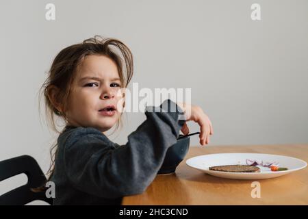 Une fillette malheureuse mange de la soupe dans un bol noir avec du pain et de l'oignon.Photo de style de vie d'un enfant dans la cuisine ayant un repas, hurlant enfant.Mangeur difficile Banque D'Images