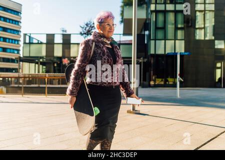Italie, femme senior à la mode transportant un skateboard en ville Banque D'Images
