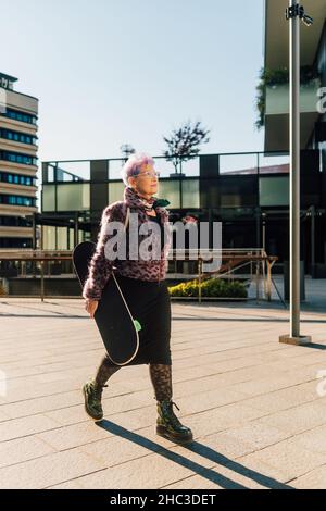 Italie, femme senior à la mode transportant un skateboard en ville Banque D'Images