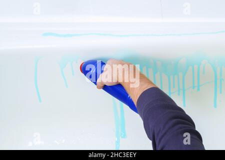 Un homme applique un nettoyant pour le bain et frotte le bain avec une brosse, un chiffon.Nettoyage de la salle de bains. Banque D'Images