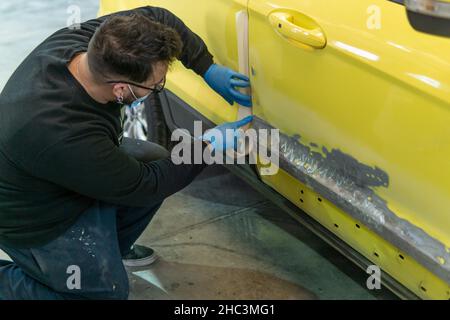 Mécanicien automobile répare une voiture jaune pour la peinture dans un atelier Banque D'Images