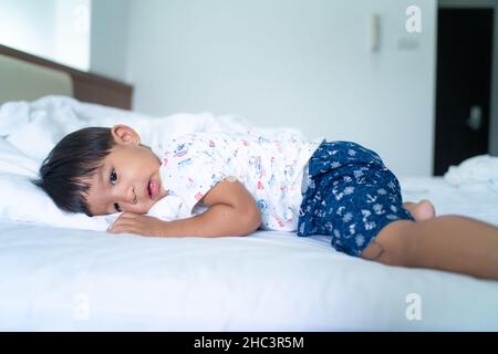 Un petit garçon dorme sur son lit le matin, se réveille avec une couverture blanche Banque D'Images