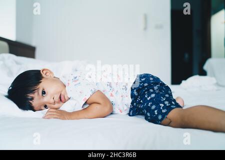 Un petit garçon dorme sur son lit le matin, se réveille avec une couverture blanche Banque D'Images