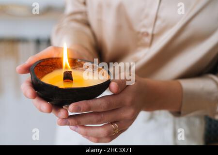 Gros plan court de jeune femme méconnaissable tenant une bougie parfumée à la main dans les mains. Banque D'Images