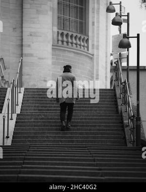 Plan vertical en niveaux de gris de l'homme grimpant les escaliers. Banque D'Images