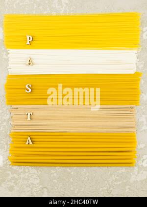 Vue verticale sur le dessus de plusieurs pâtes italiennes sèches sur fond gris. lettres en bois avec le mot « pâtes » Banque D'Images