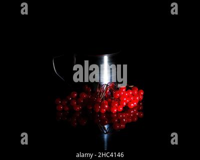 Tasse de thé en métal avec baies de viburnum dans l'obscurité. Banque D'Images
