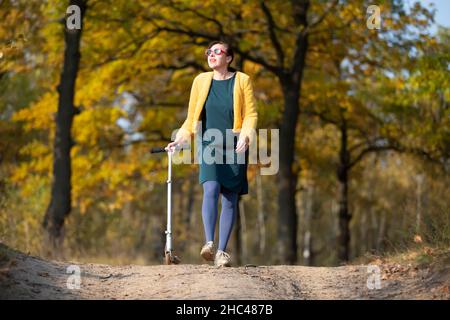 Une belle femme d'âge moyen marche avec un scooter en automne. Banque D'Images