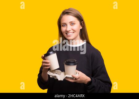 Portrait d'une jolie fille gaie portant deux tasses en papier sur fond jaune Banque D'Images