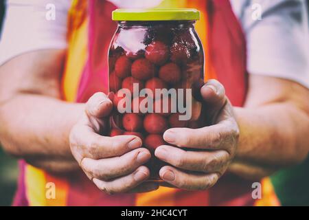 Femme âgée tenant un pot de compote de cerises.Délicieuses cerises en conserve faites maison dans un pot en verre. Banque D'Images