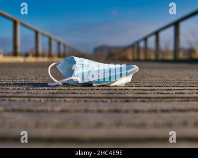 Un masque en plastique bleu jeté sur une promenade en bois dans une campagne rurale.Les mains courantes mènent au point de fuite contre un ciel bleu. Banque D'Images