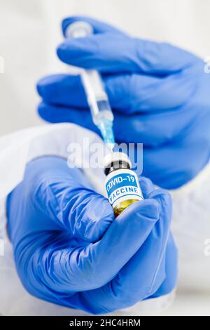 Gros plan de la main dans des gants pour la préparation de la dose de vaccin COVID-19 à partir d'un flacon en verre et l'injection de la seringue de remplissage pour la vaccination, le médecin NHS ou le médicament Banque D'Images