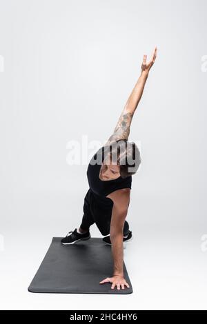 Un sportif tatoué qui fait une planche latérale sur un tapis de fitness sur fond gris Banque D'Images