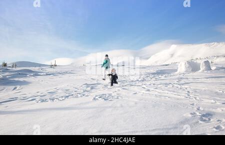 la famille, la mère et l'enfant heureux dans des vêtements chauds ont plaisir à l'extérieur, courir joyeusement dans la neige pendant un hiver ensoleillé froid dans les montagnes.Profitez-en Banque D'Images