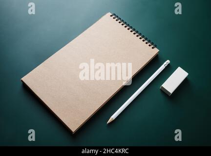 Photo d'un carnet de croquis kraft vierge, d'un crayon et d'une gomme sur fond vert.Modèle d'identité de marque. Banque D'Images