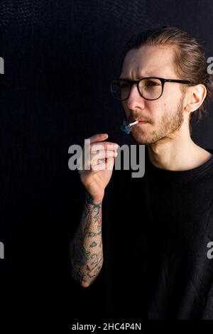 Woodbridge Suffolk UK Mai 08 2020: Un jeune hipster mâle fuyant une cigarette roulée à la main ou une articulation de cannabis Banque D'Images