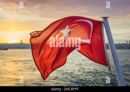 Le drapeau turc flotte dans le vent contre le Bosphore d'Istanbul au coucher du soleil.Le drapeau de la République de Turquie. Banque D'Images