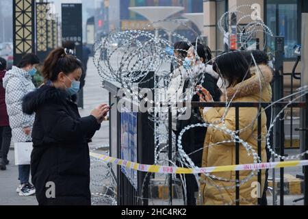 XI'AN, CHINE - 24 DÉCEMBRE 2021 - les résidents collectent les nécessités quotidiennes achetées en ligne dans une communauté fermée avec barbelé installé à la porte dans Banque D'Images