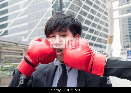 Un jeune homme d'affaires asiatique frappe avec un gant de boxe rouge dans la ville Banque D'Images