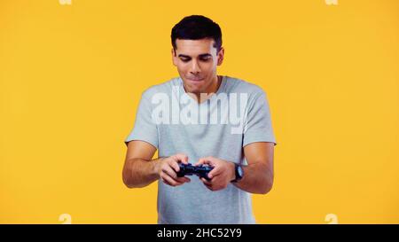 KIEV, UKRAINE - 22 DÉCEMBRE 2021: Jeune homme joyeux regardant le joystick et les lèvres mordant isolées sur le jaune Banque D'Images