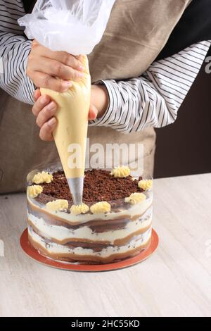 Le confiseur au travail.Gâteau à la crème décoratif.Faire cuire la table préparer un gâteau Tiramisu sur fond brun. Banque D'Images