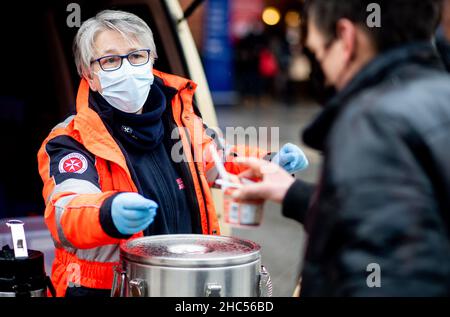 Brême, Allemagne.24th décembre 2021.Karin Stelljes, chef d'équipe au bus froid Johanniter, remet un repas chaud à une personne dans le besoin la veille de Noël sur la piste de la gare principale.À plusieurs endroits à Brême, des repas chauds ou des sacs avec de la nourriture et des cadeaux sont distribués aux sans-abri et aux personnes dans le besoin à la veille de Noël.Credit: Hauke-Christian Dittrich/dpa/Alay Live News Banque D'Images