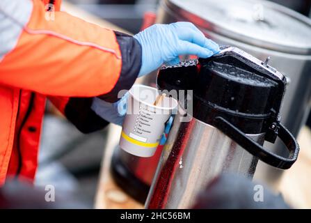 Brême, Allemagne.24th décembre 2021.Karin Stelljes, chef d'équipe au bus Johannitre pour temps froid, remplit une tasse de café pour une personne dans le besoin la veille de Noël sur la piste de la gare principale.À plusieurs endroits de Brême, des repas chauds ou des sacs avec de la nourriture et des cadeaux sont distribués aux sans-abri et aux personnes dans le besoin à la veille de Noël.Credit: Hauke-Christian Dittrich/dpa/Alay Live News Banque D'Images