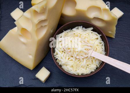 Des quartiers de fromage hollandais et un bol de fromage râpé sur un plateau de pierre noire. Banque D'Images