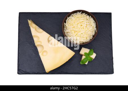 Coin de fromage hollandais et un bol de fromage râpé avec des feuilles de basilic sur une plaque de pierre d'ardoise noire isolée sur blanc. Banque D'Images