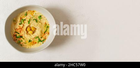 Houmous dans un bol blanc en céramique avec paprika et feuilles de persil sur fond clair.Bannière.Un plat traditionnel du Moyen-Orient.Orientation horizontale Banque D'Images