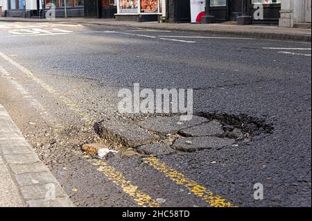 Vue à angle bas d'un grand nid d'poule causant des dommages sur le côté d'une route Banque D'Images