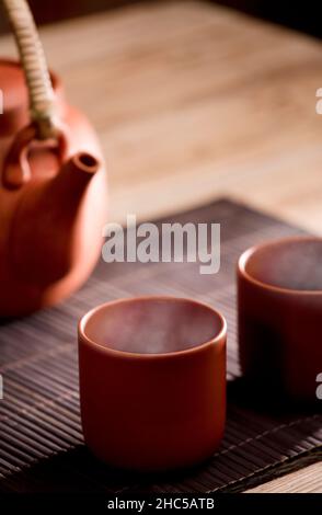 Deux tasses de thé chaud en argile brune ou de café, sur une table en bois avec vue partielle sur la bouilloire ou la cafetière. Fond marron.Espace pour le texte. Banque D'Images