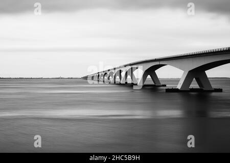 Photo en niveaux de gris du pont de Zeeland au-dessus de la rivière calme sous un ciel clair, les pays-Bas Banque D'Images