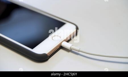 Gros plan de l'iPhone Apple avec le câble de charge posé sur la table blanche.Processus de charge d'un appareil moderne connecté à un câble usb. Banque D'Images