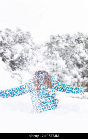 Jeune femme, s'amuser en jetant de la neige dans les airs, lors d'une promenade dans une forêt enneigée, tir vertical Banque D'Images