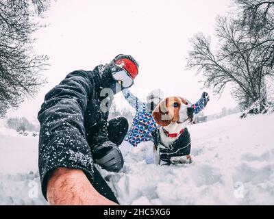 Couple heureux avec leur chien beagle, prenant un selfie pendant une tempête de neige, équipé de vêtements d'hiver, de gros plan, concept de vacances Banque D'Images