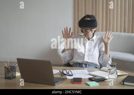 Femme d'affaires excitée portant des lunettes de réalité virtuelle pendant son travail au bureau Banque D'Images