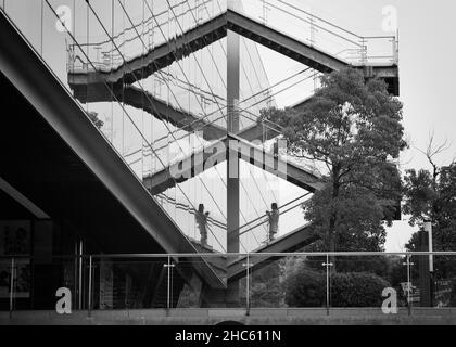 Photo d'une femme marchant dans les escaliers reflétés dans la fenêtre d'un grand bâtiment dans la photo d'en dessous, dans un immeuble de bureaux, Shang Banque D'Images