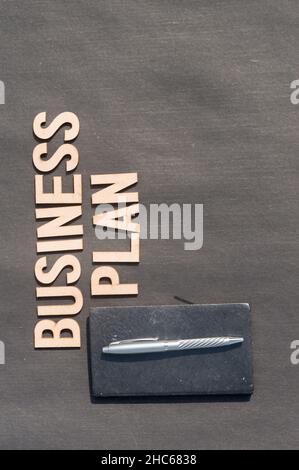 Main d'homme d'affaires plaçant un stylo et un carnet devant le plan d'affaires Word fait de blocs de bois de lettres Alphabet.Vue grand angle.Rétrogr. Vertical Banque D'Images