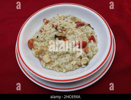 Risotto italien aux fruits de mer avec tomates cerises isolées sur fond rouge. Banque D'Images