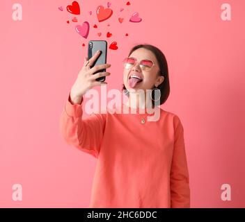 Belle jeune femme avec téléphone envoyant un message d'amour sur fond rose Banque D'Images