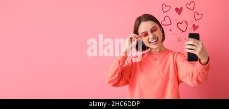 Belle jeune femme avec téléphone envoyant un message d'amour sur fond rose Banque D'Images