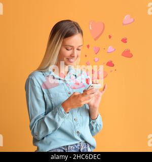 Belle jeune femme avec téléphone envoyant un message d'amour sur fond de couleur Banque D'Images