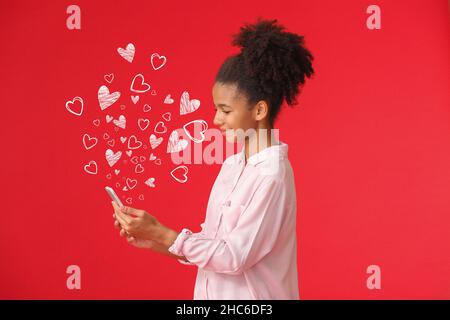 Adolescente afro-américaine avec téléphone mobile envoyant un message d'amour sur fond de couleur Banque D'Images