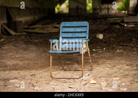 Une ancienne chaise pliante en plastique devant un entrepôt abandonné Banque D'Images