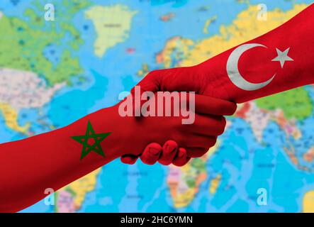 Poignée de main entre la Turquie et le Maroc drapeaux peints sur les mains.avec arrière-plan de la carte du monde Banque D'Images