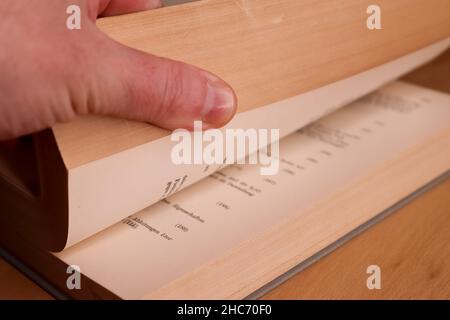 Vue sélective d'un vieux livre de mathématiques allemand épais avec une main masculine cherchant dans lui Banque D'Images